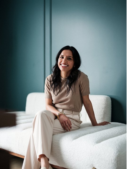 Gunjan Sud, founder of Thimble & Thread, smiling while seated on a white sofa