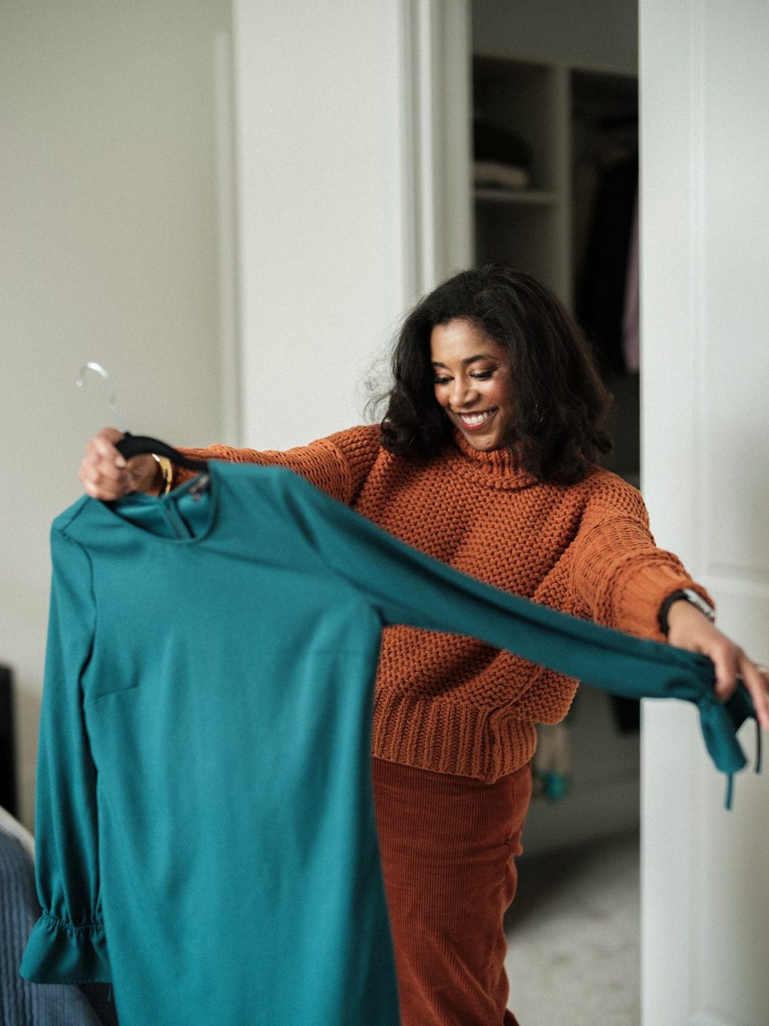 Woman smiling as she holds up a teal dress from her closet